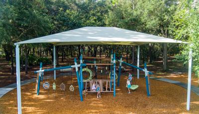 Elevated view of a large shade system over play structures with playing children.