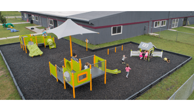 Elevated view of a play area set next to a grey building. Children play on three separate play structures colored in lime green and yellow.