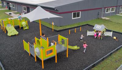 Elevated view of a play area set next to a grey building. Children play on three separate play structures colored in lime green and yellow.