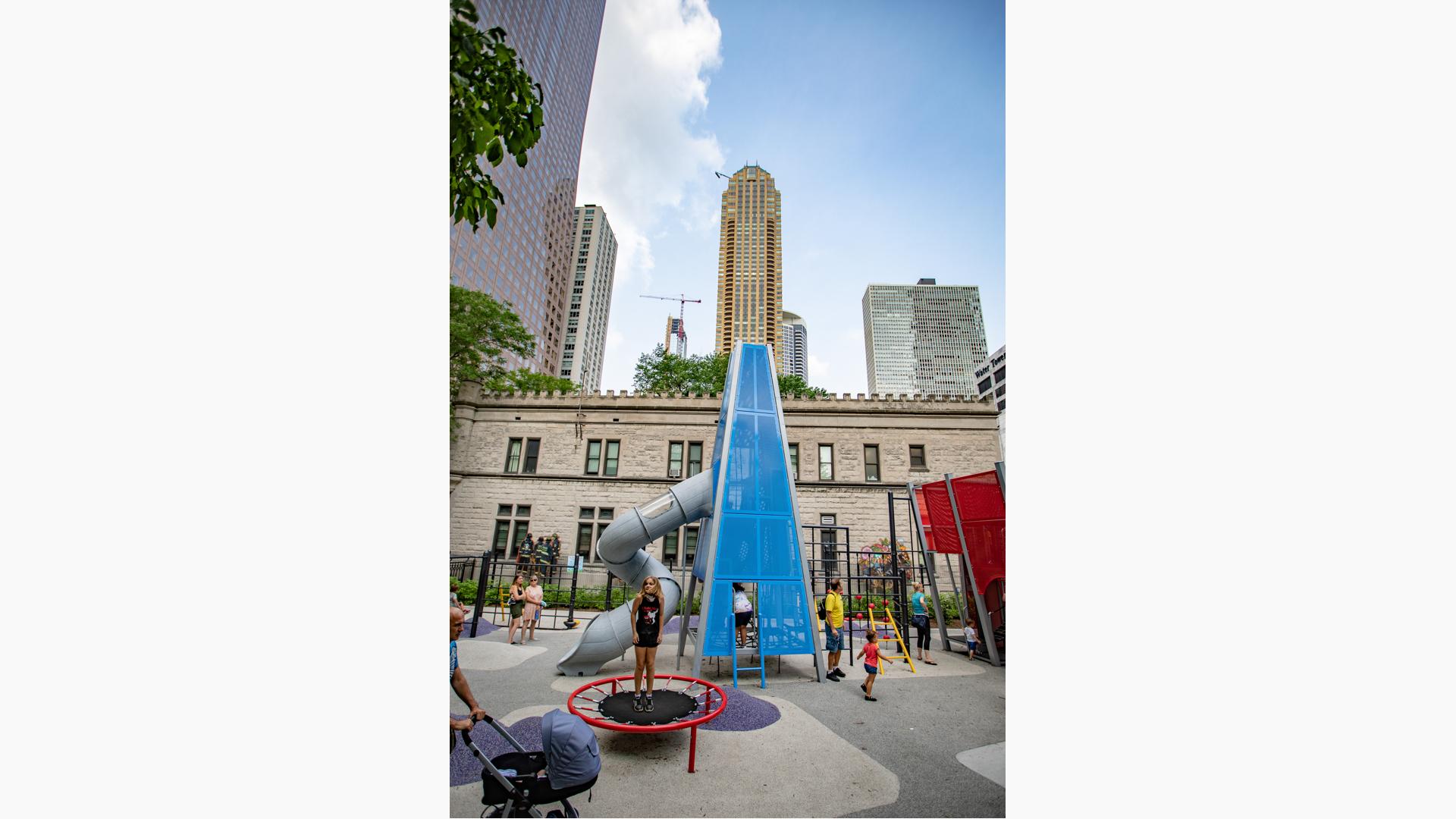 Girl standing on trampoline next to blue custom play structure