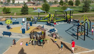 Children and families play on a sunny day in this alien-themed park. Featuring a UFO roof and a solar system sculpture in the middle of the playground.