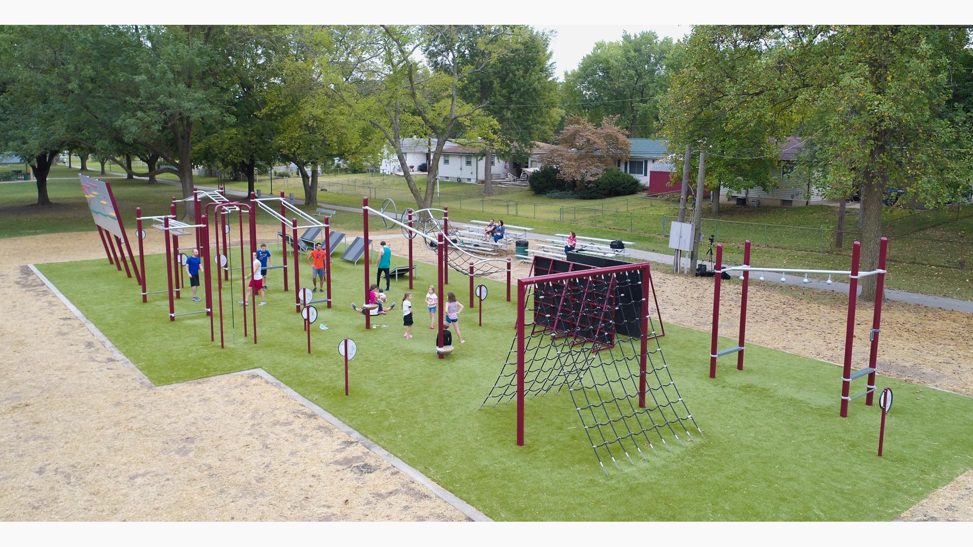 Adult and kids are ready for the challenges of Howdershell FitCore® Park. Parked on a patch of green grass, men stand under different freestanding structures to test their agility.