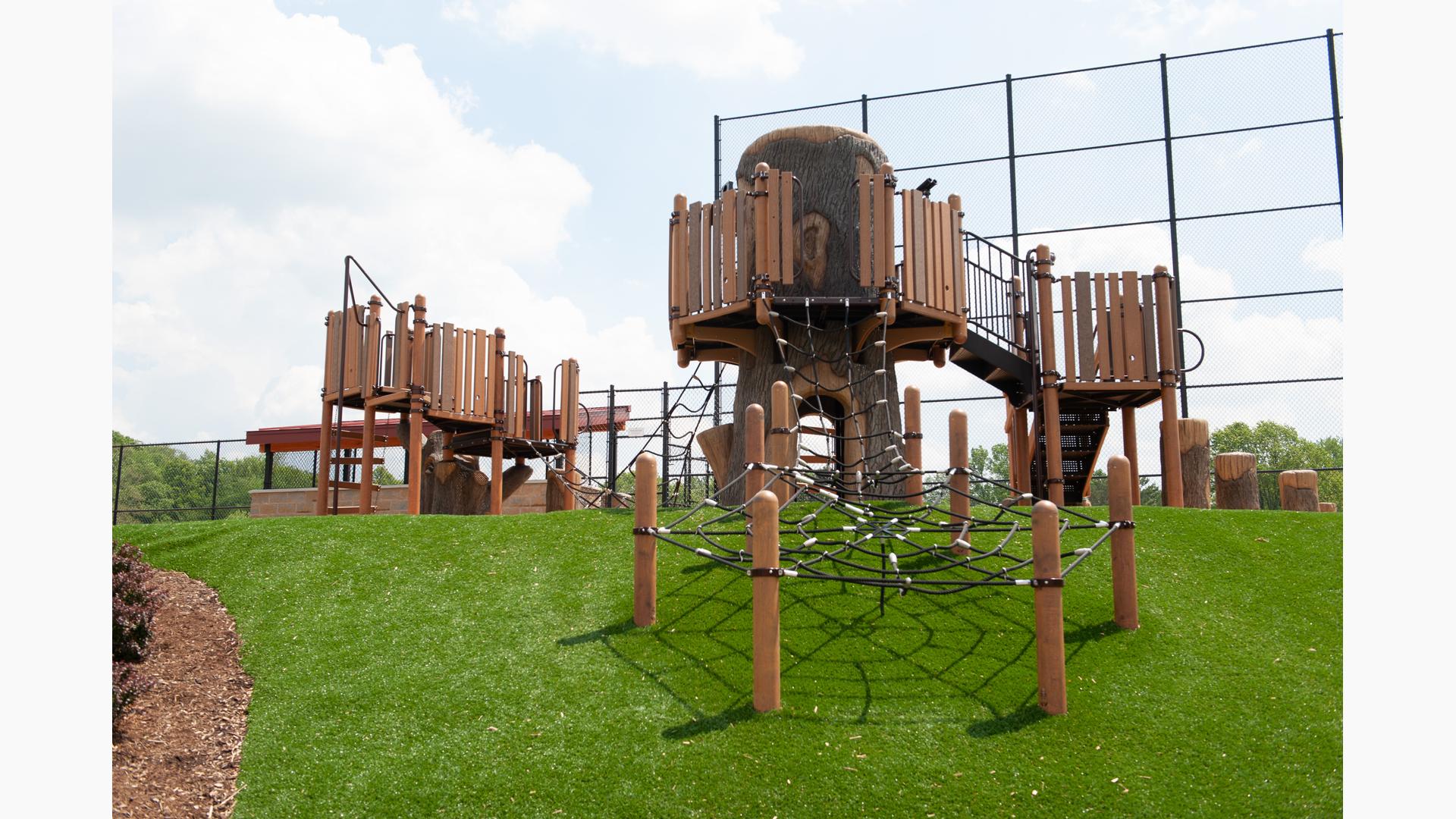 Custom treehouse fort in Rossford Park with net climbers going down hillside.