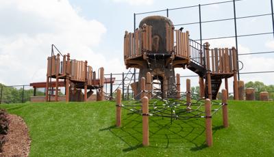 Custom treehouse fort in Rossford Park with net climbers going down hillside.