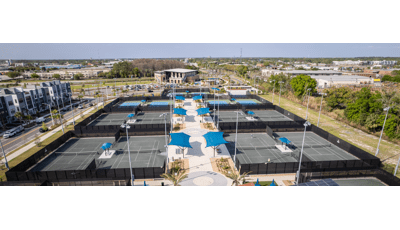 Full elevated view of enclosed tennis courts with player shade seating areas between courts and spectator shade systems on the sides of the courts.