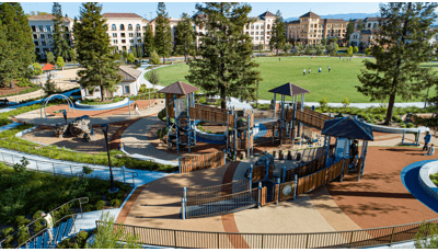 Elevated view of a large inclusive playground designed with recycled wood-grain paneling in a large park surrounded by apartment buildings.