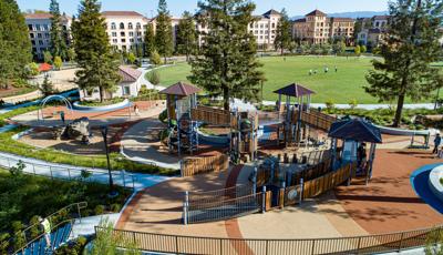 Elevated view of a large inclusive playground designed with recycled wood-grain paneling in a large park surrounded by apartment buildings.