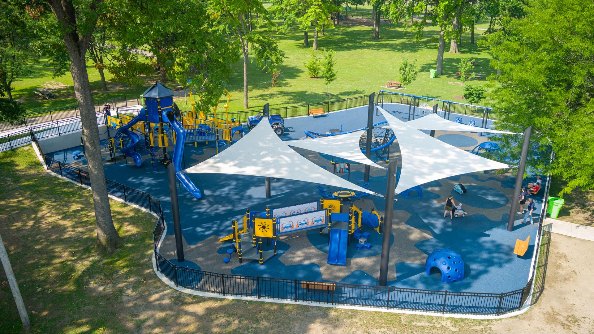 Elevated view of a park playground with multiple large shade sails covering one portion of the play area.