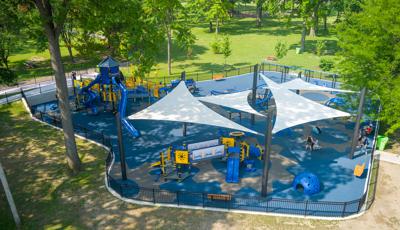 Elevated view of a park playground with multiple large shade sails covering one portion of the play area.