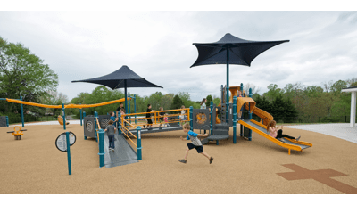 Inclusive PlayBooster® play structure is perfect for children of all abilities. Children run in a line up the ramps to the slides. A custom surface features a cross stretched out on the ground.