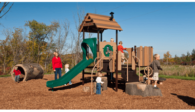 Mom watches children play on nature-inspired PlayShaper play structure on a sunny day.