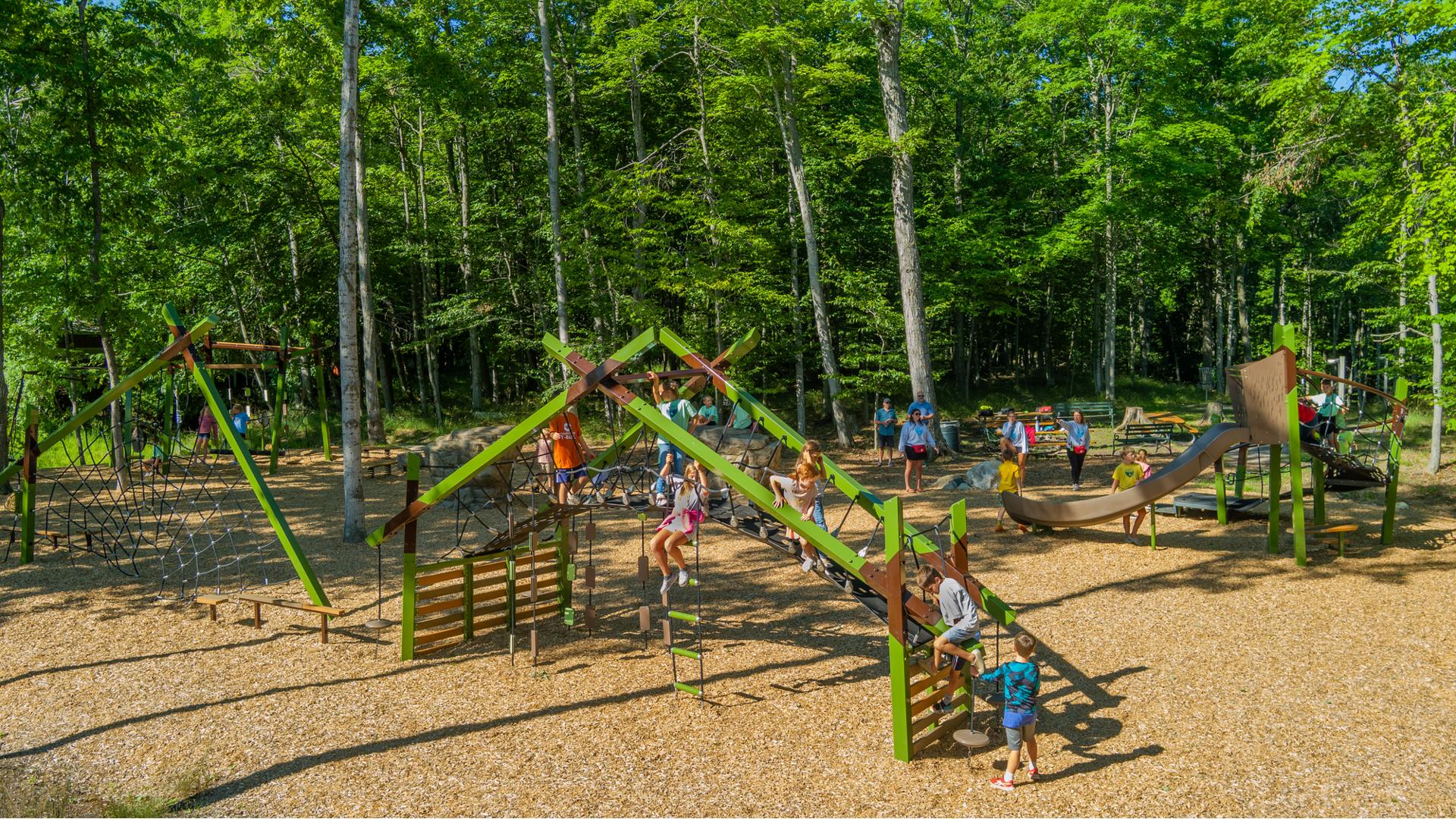 Elevated view of a park playground nestled next to a lush line of trees.