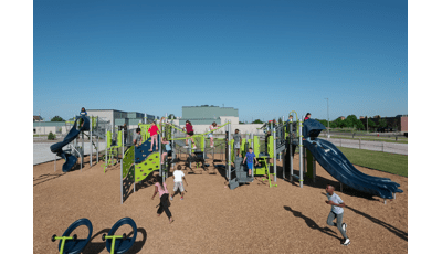 Children of Willow Park Elementary playing on new play structure. A large group climb on the Cascade climber. Two girls walk across net bridge. The line for the double slide is 3 kids deep as a boy runs across playground.