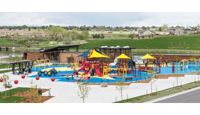 Full view of a park inclusive playground next to a pond with ramps, slides, swings, climbers, and overhead shade accessible to all ages.