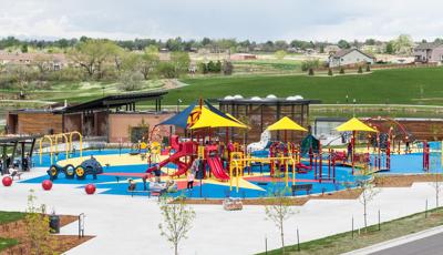 Full view of a park inclusive playground next to a pond with ramps, slides, swings, climbers, and overhead shade accessible to all ages.