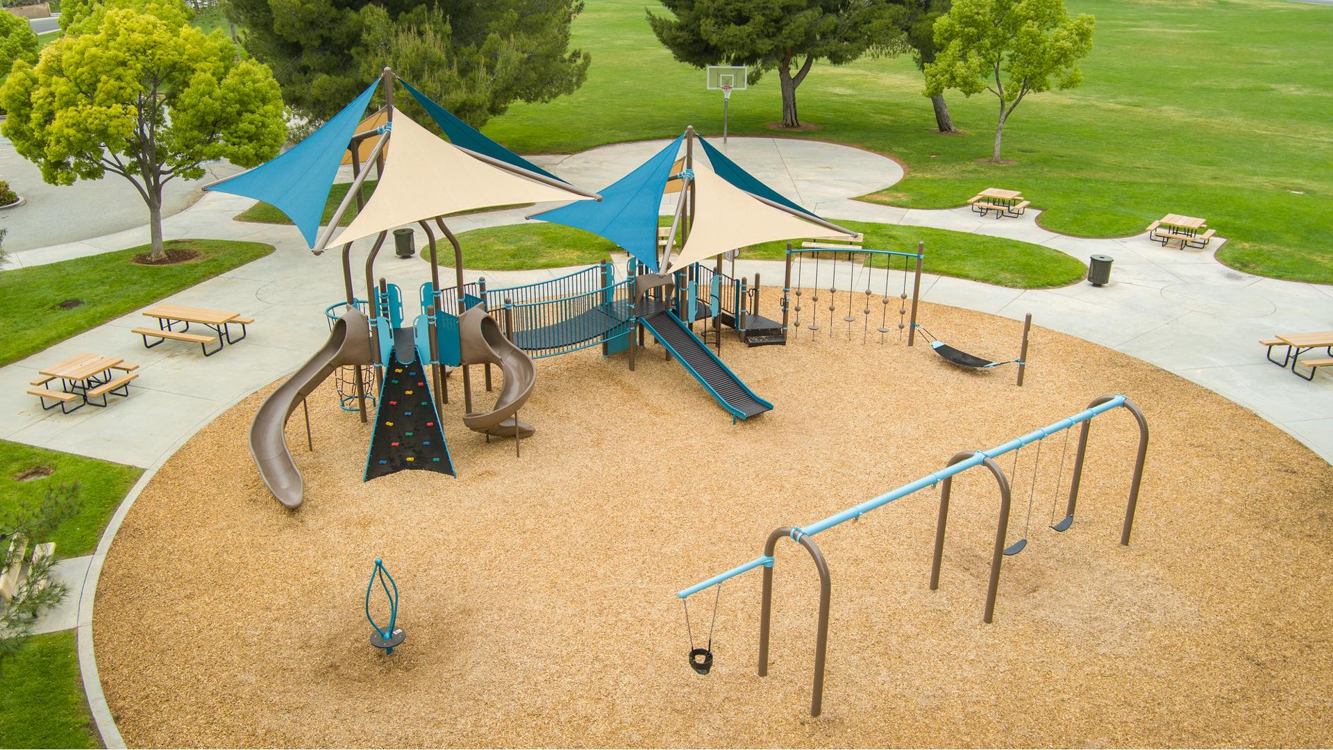 Elevated view of a circular play area with main play structure, swing set, and stand up spinner at a town park.