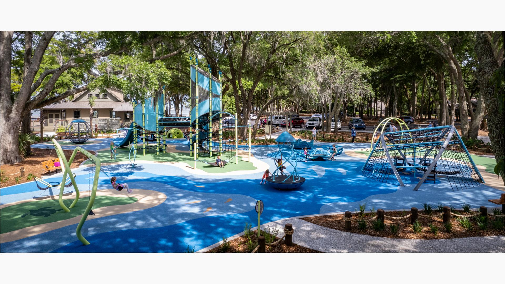 Large trees surrounded a play area with two main play structures as children play on other swings and playground spinners.