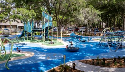 Large trees surrounded a play area with two main play structures as children play on other swings and playground spinners.