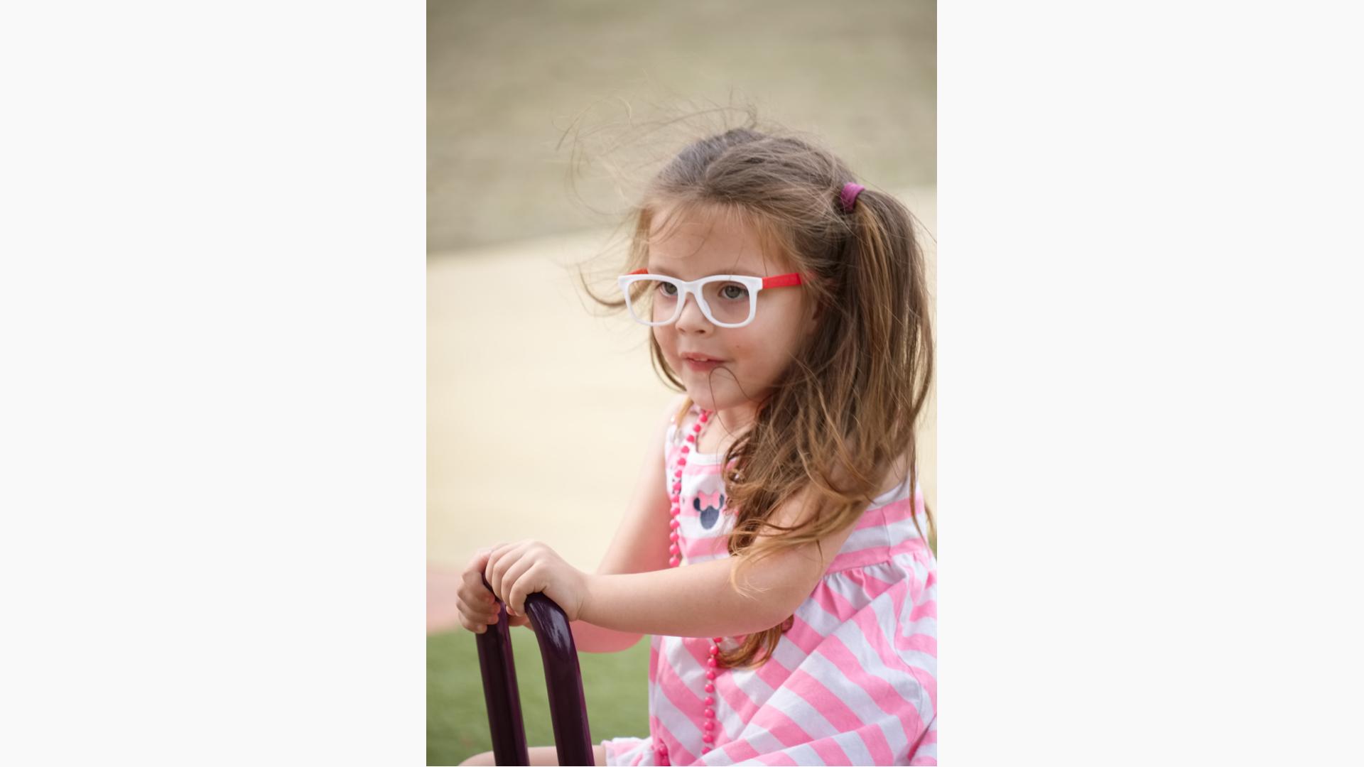 Girl wearing glasses and pink stripe dress sitting on see-saw