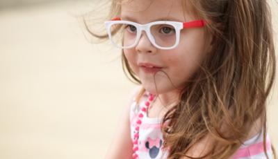 Girl wearing glasses and pink stripe dress sitting on see-saw