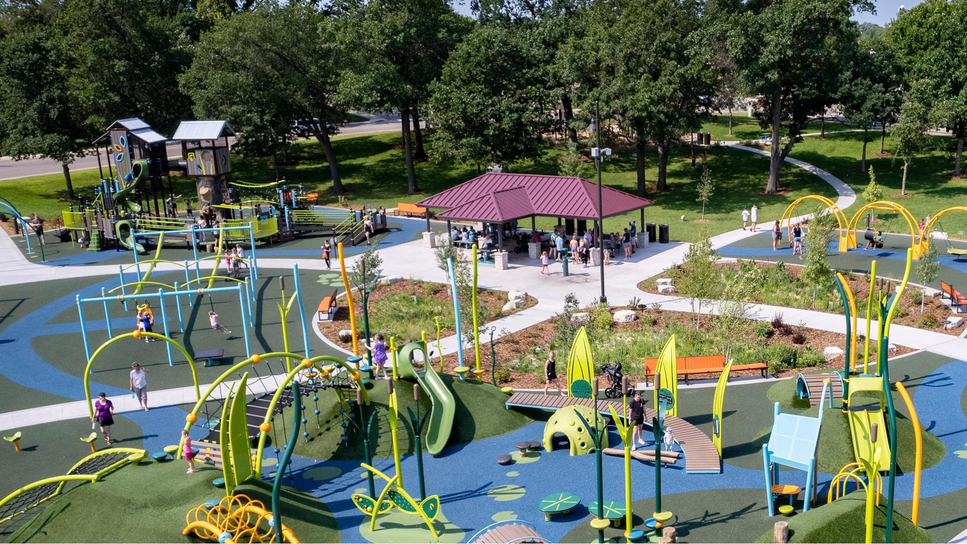 Elevated view of a large park play area with a nature inspired theme and a pavilion rest area with picnic tables.