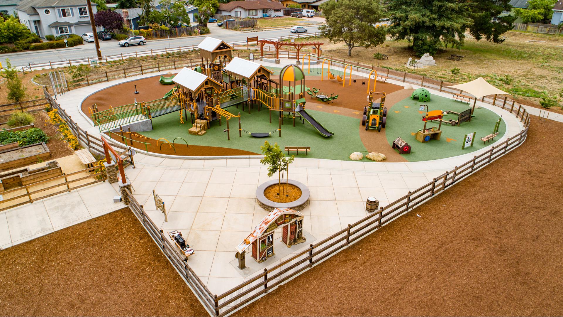 Elevated view of a farm themed inclusive play area with tractor climber, barn themed sensory wall, and large barn themed play structure.