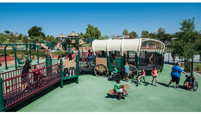 Children playing in wheelchairs on this accessible ramped western-themed playground. Playground design as wagon-covered structure and spring riders designed as a horse. 