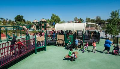 Children playing in wheelchairs on this accessible ramped western-themed playground. Playground design as wagon-covered structure and spring riders designed as a horse. 