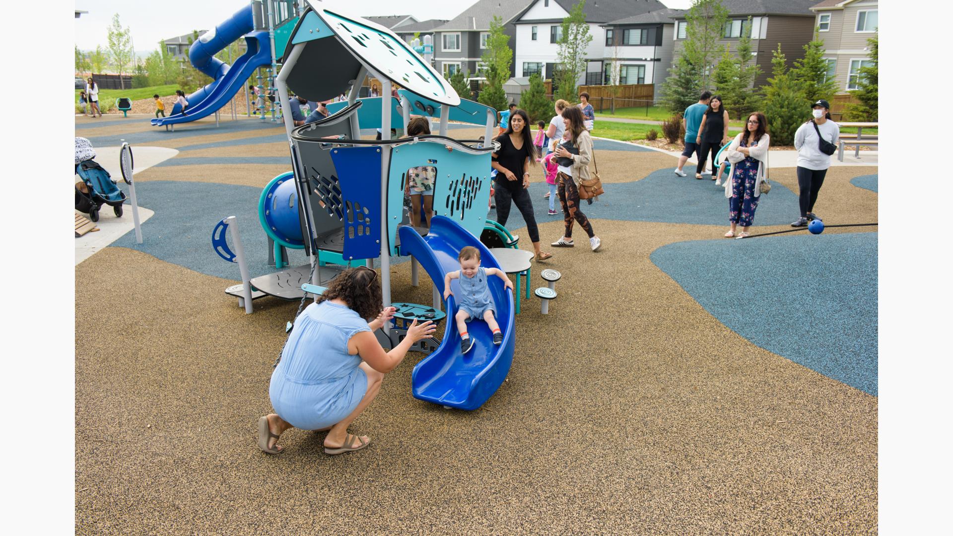 Boy happily rides down slide to woman