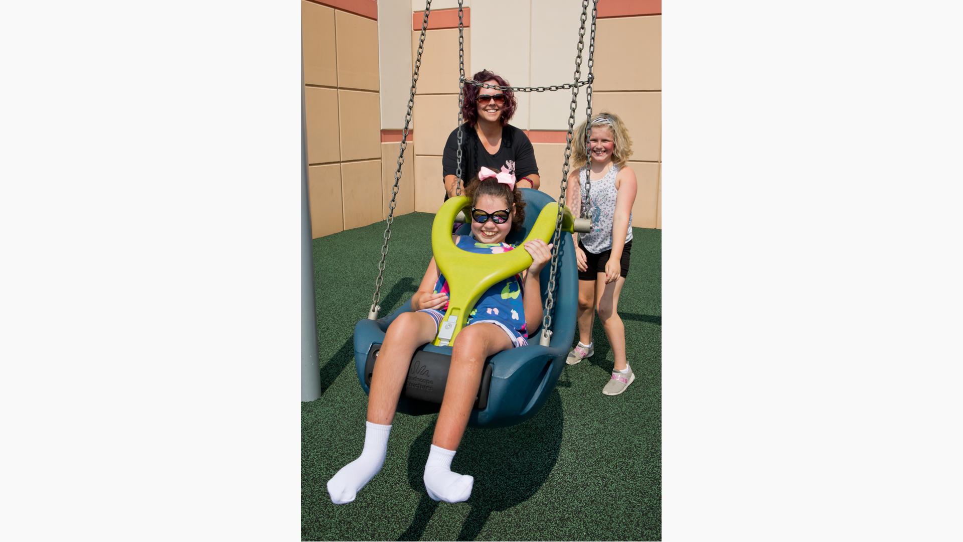 Family having fun pushing girl in Molded Bucket Seat (5-12 yrs) w/Harness and w/Chains