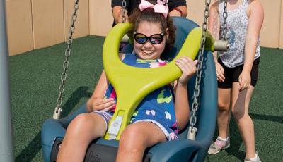 Family having fun pushing girl in Molded Bucket Seat (5-12 yrs) w/Harness and w/Chains