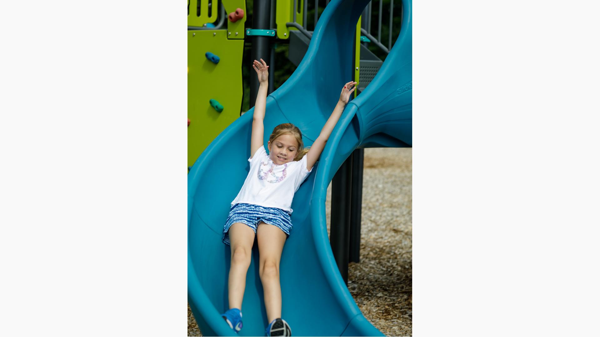 Girl rides down slide with arms up in the air