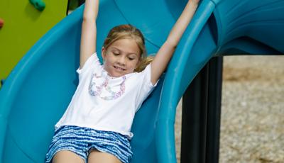 Girl rides down slide with arms up in the air