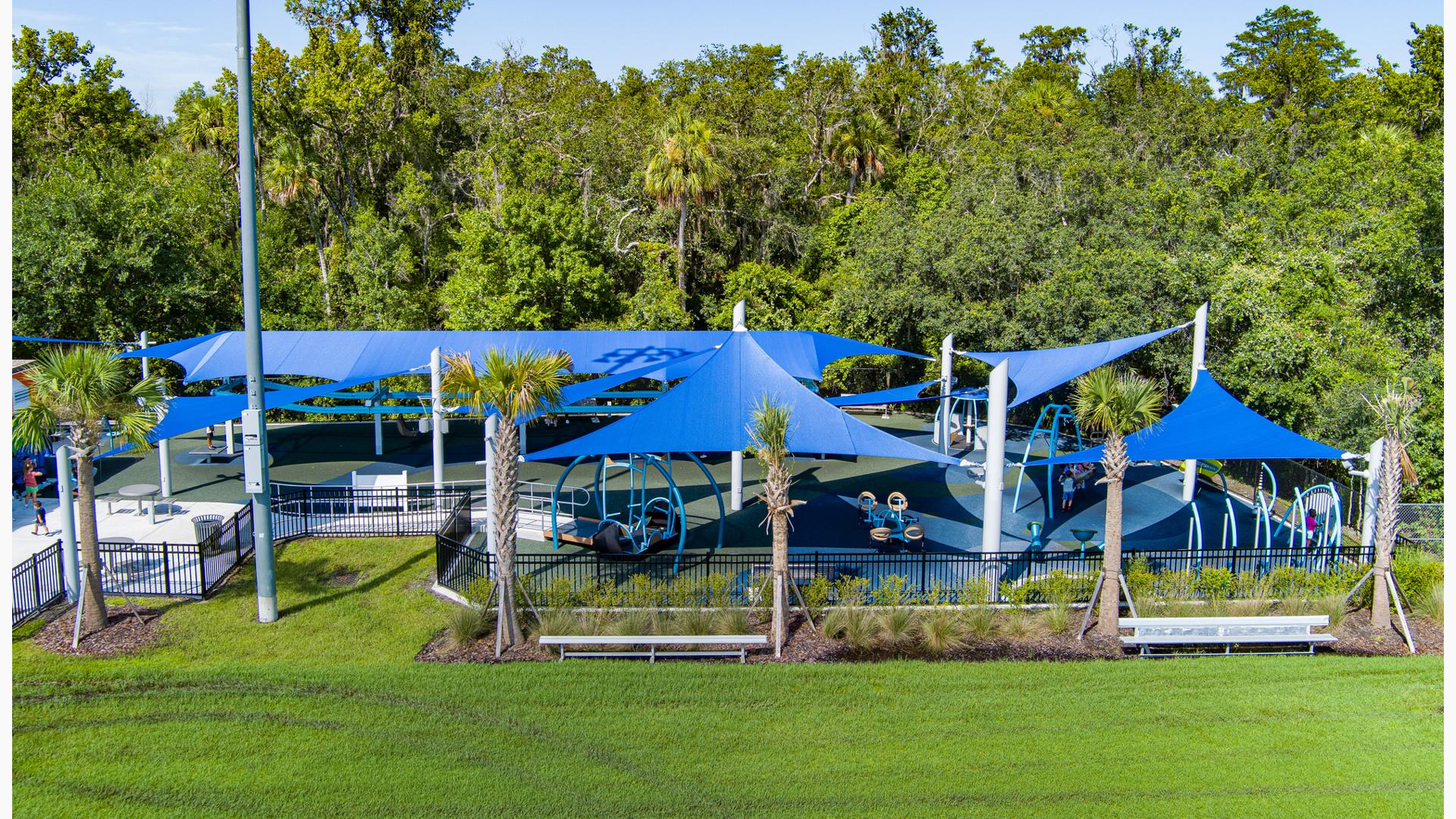 Elevated view of an enclosed play area with large blue shades covering the entire play area all next to wooded tree line.