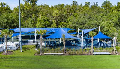 Elevated view of an enclosed play area with large blue shades covering the entire play area all next to wooded tree line.