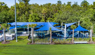 Elevated view of an enclosed play area with large blue shades covering the entire play area all next to wooded tree line.