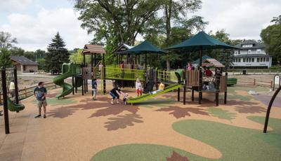 Nature-inspired playground with kids playing and parents joining in. Surfacing includes a leaf design colored in green and brown. 
