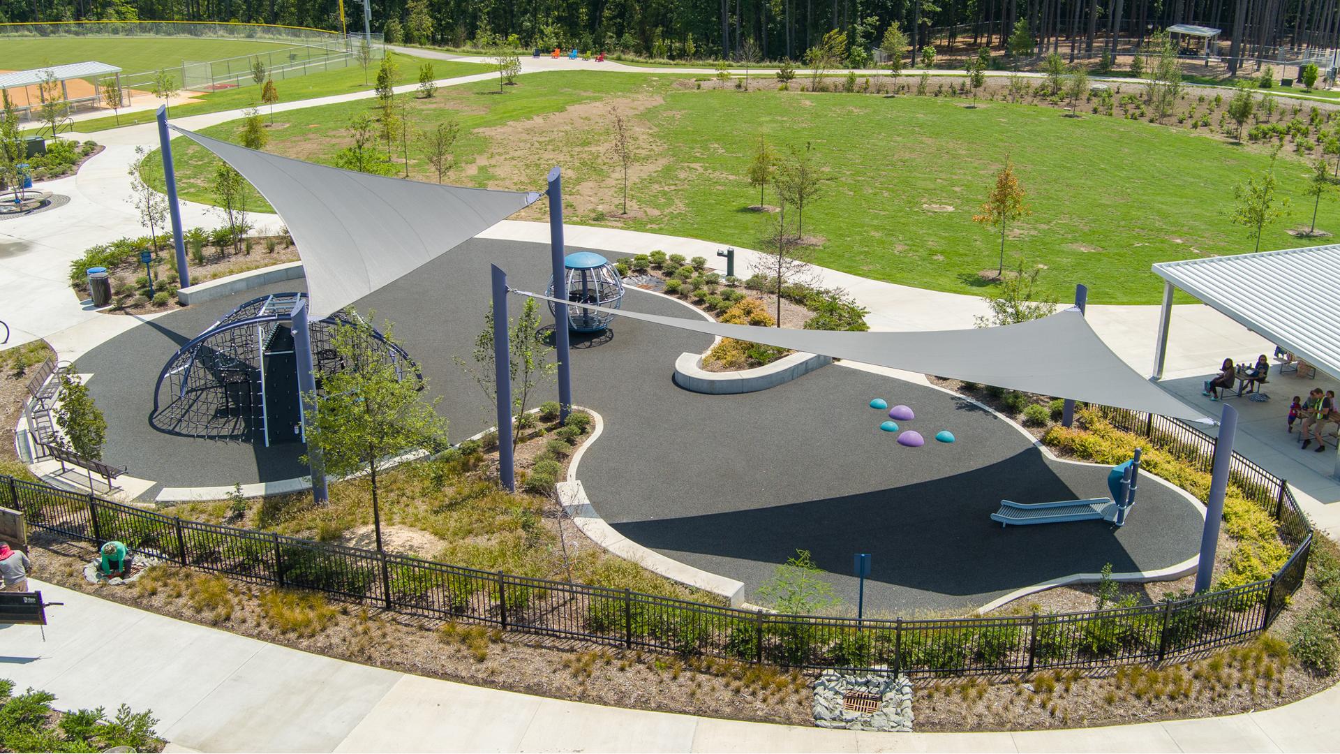 Elevated view of large gray shade sails cover a play area with a domed climbing structure and a large globe multi-person spinner.