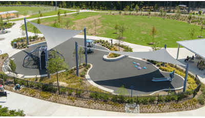 Elevated view of large gray shade sails cover a play area with a domed climbing structure and a large globe multi-person spinner.