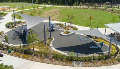 Elevated view of large gray shade sails cover a play area with a domed climbing structure and a large globe multi-person spinner.