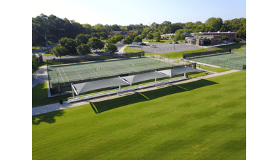 俯瞰郁郁葱葱的绿色田野，人行道上有一排排由三个大型矩形遮阳系统覆盖的看台，后面有三个网球场的围栏。