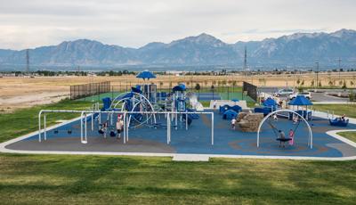 This playground is named for a 6-year-old kidnapping victim from West Jordan, Utah. The community wanted to bring awareness to child abuse and also provide a place where children of all abilities can play together. Two children play on the Oodle swing, while a family enjoy a swing. The mountains sit on the horizon overlooking the playground.