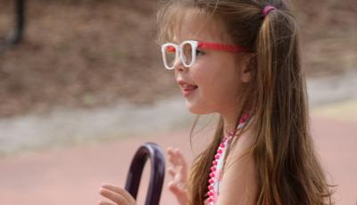 Girl wearing pink stripe dress and glasses stands next to see-saw