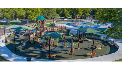 Families play at a large play space on a jungle themed playground with  brown posts and green accents and matching near by splash pad. 