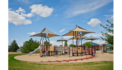 Sports-themed playground with grey and brown multi-panel shade covering the playground.  Surfacing is designed like a baseball. 