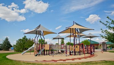 Sports-themed playground with grey and brown multi-panel shade covering the playground.  Surfacing is designed like a baseball. 