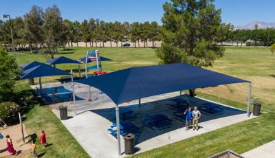 Several navy blue shade structures cover picnic tables and also benches at a splash pad that includes an American flag painted on a dumping bucket along with ground sprays. 