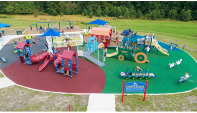 Elevated view of a play area with multiple farm themed play structures. One structure is designed like a red barn while another a green tractor. 