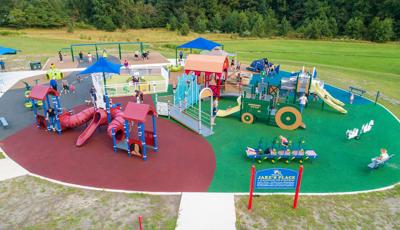 Elevated view of a play area with multiple farm themed play structures. One structure is designed like a red barn while another a green tractor. 