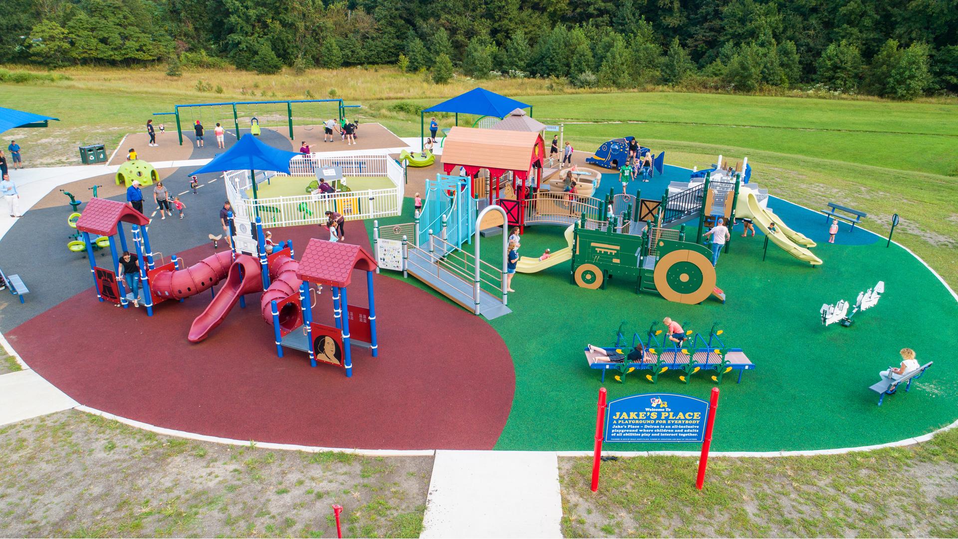 Elevated view of a play area with multiple farm themed play structures. One structure is designed like a red barn while another a green tractor. 